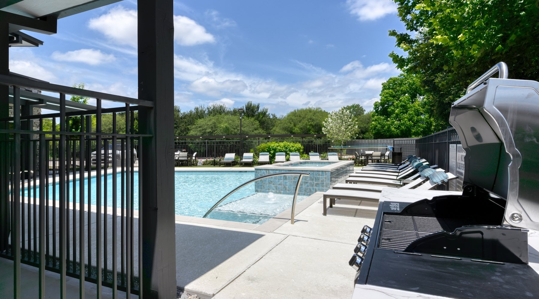 a grill area in front of a pool with lounge chairs